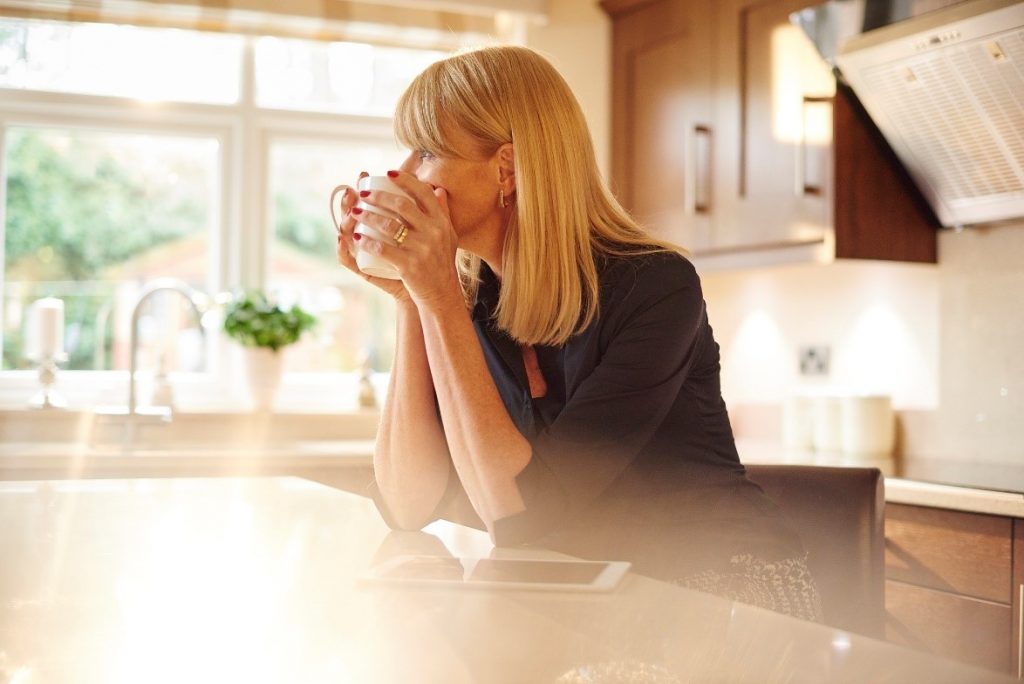 middle-age woman standing at kitchen counter with coffee mug staring blankly into the distance