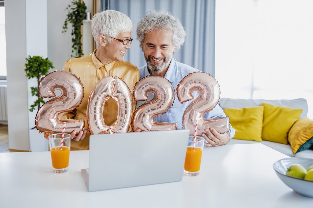 Senior woman and senior man at home holding 2022 balloon numbers and chatting on a video call